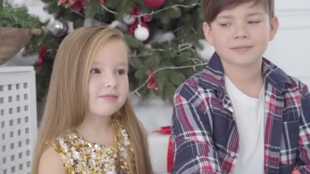 Close-up portret van blanke jongen zoenen schattig meisje op wang onder kerstboom. Oudejaarsavond, eerste liefde, geluk. — Stockvideo