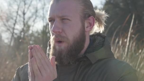 Felnőtt fehér férfi portréja, amint napfényben áll és kézen fúj. Fagyott férfi turista dörzsöli a kezét. Életmód, utazás, turizmus. — Stock videók