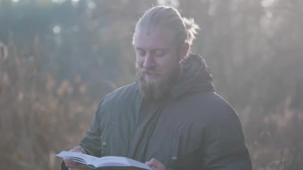 Portrait of handsome Caucasian man with grey eyes and beard standing in autumn forest and reading. Happy tourist enjoying resting outdoors. Leisure, lifestyle, hobby. — 비디오