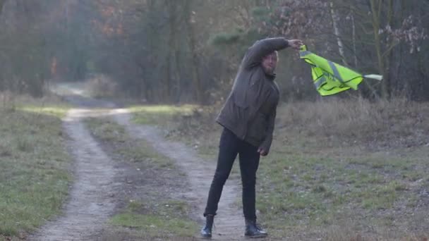 Retrato del hombre caucásico guapo en el bosque de otoño sacudiendo chaleco verde como de pie en el camino del bosque. Turista masculino viajando solo. Autoestop, turismo, hobby . — Vídeos de Stock