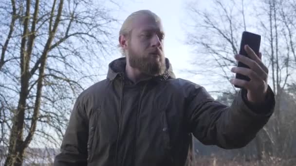 Уверенный взрослый европеец, стоящий в осеннем лесу перед озером и делающий селфи. Счастливый турист использует свой смартфон, чтобы сфотографировать. Стиль жизни, хобби, досуг . — стоковое видео