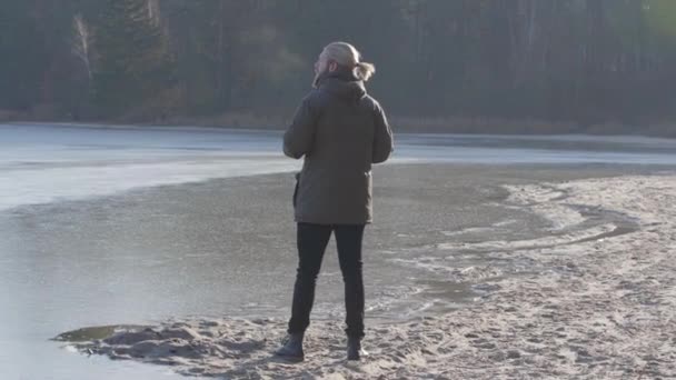 Vista trasera del solitario hombre caucásico de pie en la orilla del lago y mirando hacia otro lado. Turista seguro disfrutando de un soleado día de otoño al aire libre. Ocio, estilo de vida, viajes . — Vídeos de Stock