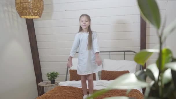 Porträtt av glada lilla vita flicka som har roligt hemma. Glada barn dansar och hoppar på sängen inomhus. Livsstil, barndom, lycka. — Stockvideo