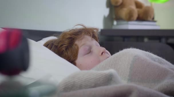 Zijaanzicht van kleine roodharige blanke jongen verstopt onder een deken. Verschrikt schattig kind bang om alleen te zijn. Stress, jeugd, levensstijl. — Stockvideo