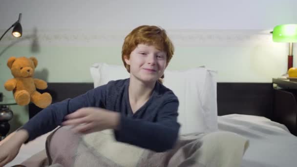 Headshot de mignon petit garçon caucasien changer de chaînes, ce qui rend l'expression faciale intéressée, et regarder la télévision. Enfant rousse à la recherche de dessins animés intéressants. Enfance, loisirs, coucher . — Video