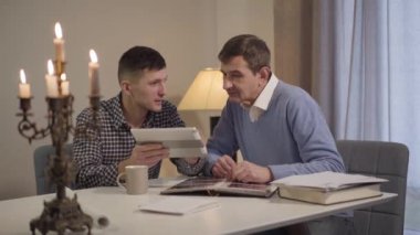 Yetişkin beyaz bir çocuğun orta yaşlı bir babaya tablet kullanmayı öğrettiği portresi. İnternette nasıl sörf yapılacağını ailesine gösteren bir adam. Nesiller, yaşam tarzı, aile.