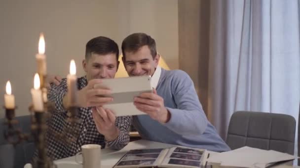 Porträtt av en vit vuxen far och son som kramas och tar selfie på tabletter. Glad medelålders man och glad kille vilar tillsammans hemma på kvällen. Livsstil, fritid, bindning. — Stockvideo