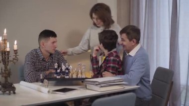 Güzel, neşeli, beyaz bir kadın içeride satranç oynayan erkeklere geliyor. Olumlu orta yaşlı büyükanne koca, oğul ve torunla konuşuyor. Mutlu bir aile akşamları evde dinleniyor..