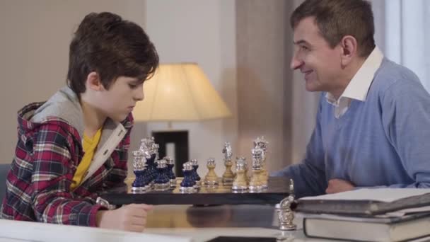 Маленький кавказький хлопчик і чоловік середнього віку грають у шахи. Дідусь і онук проводили вечір разом удома. Спосіб життя, дозвілля, хобі. — стокове відео