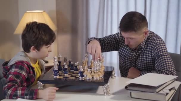 Portrait of young Caucasian father playing chess with son in the evening. Intelligent man teaching son to play. Lifestyle, joy, happiness. — 비디오