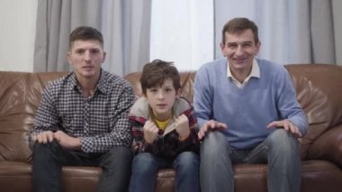 TV 'de maç izleyen çok nesilli bir futbol taraftarı ailenin portresi. Orta yaşlı bir adam, yetişkin oğlu ve küçük torunu kazanırken zafer jestleri yapıyorlar. Hobi, eğlence..