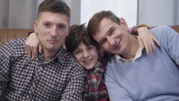 Ritratto ravvicinato di tre uomini caucasici di età diverse che guardano la macchina fotografica e sorridono. Nonno, figlio e nipote che posano in casa. Felicità, famiglia, stile di vita . — Video Stock