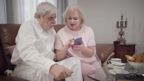 Moderne oudere blanke vrouw die haar elegante man leert smartphone te gebruiken. Intelligente volwassen vrouw gepensioneerd zitten met de telefoon en praten met de echtgenoot. Pensioen. moderne technologieën, ondersteuning. — Stockvideo