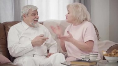 Portrait of elderly Caucasian couple arguing at home. Beautiful mature woman talking emotionally, elegant senior man explaining something to wife. Conflict, problem, relationship, lifestyle.