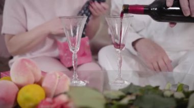 Close-up of mature male Caucasian hands pouring wine into wineglasses. Senior unrecognizable married couple celebrating Saint Valentines Day at home. Holiday, celebration, eternal love concept.
