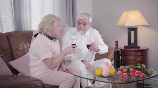 Ώριμο ζευγάρι καυκάσιων γυαλιών και πίνοντας κρασί την ημέρα του Αγίου Βαλεντίνου. Ευτυχισμένο ζευγάρι ηλικιωμένων συνταξιούχων που γιορτάζουν τις διακοπές τους σε εσωτερικούς χώρους. Ειδύλλιο, αιώνια αγάπη, δέσιμο, γιορτή. — Αρχείο Βίντεο