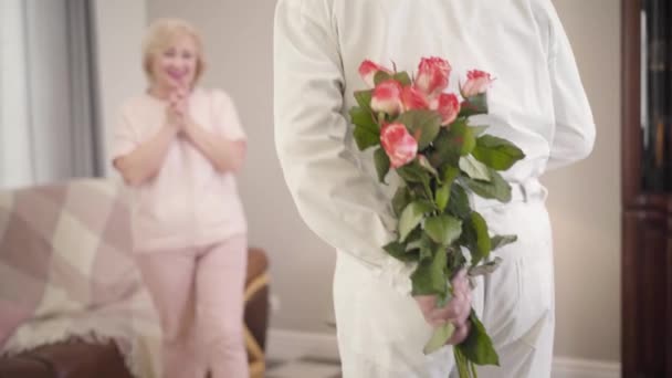 Powrót widok elegancki dojrzały mężczyzna kaukaski daje bukiet róż do pięknej żony w święto Walentynki. Starszy emerytowany mąż robi niespodziankę dla małżonka na wakacjach. Uroczystość, wieczna miłość. — Wideo stockowe