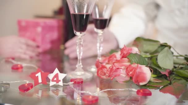 ガラスのテーブルの上に立つバラとワイングラスの花束のクローズアップ。背景には熟年男性の手でシニア妻をヤシ。高齢者の団結,聖バレンタインデー,永遠の愛. — ストック動画