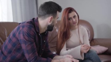 Arka plandaki bulanık saçlı kadından alyansı alan umutsuz, beyaz bir adamın yan görüntüsü. Boşanan genç evli çift. Ayrılık, evlilik sorunları, yaşam tarzı.