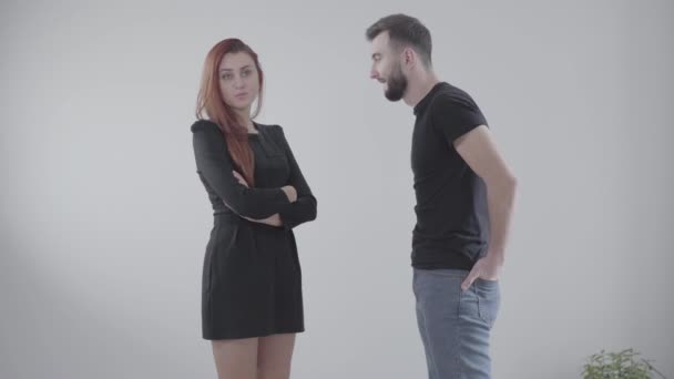 Young handsome Caucasian man and annoyed redhead woman arguing as standing at white background. Elegant girl in dress and guy in casual clothing yelling at each other indoors. Conflict, relationship. — Stock Video