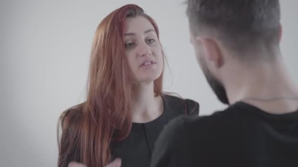 Close-up face of young irritated redhead woman arguing with unrecognizable husband or boyfriend. Two people quarreling at white background. Lifestyle, problem. conflict. — Stock Video