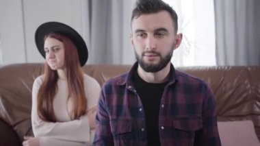 Kahverengi gözlü, kumral saçlı, elleri çapraz oturan, üzgün karısı ya da kız arkadaşı olarak arka planda ağlayan yakışıklı beyaz adamın portresi. İlişki sorunları kavramı, ayrılık