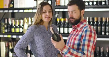 Beyaz adam ve kadın kırmızı şarabı lüks bir içki dükkanında şişelerle rafların arkasında durarak tartışıyor. Depoda içecek seçen genç bir aile. Neşe, yaşam tarzı, endüstri.