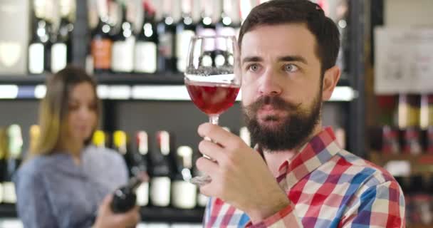 Detailní záběr soustředěného bělocha, který cítí červené víno ve skle a třese sklenicí vína. Důvěrné koncentrované sommelier degustating nápoje na luxusním trhu s alkoholem. Zaměstnání, životní styl, průmysl. — Stock video