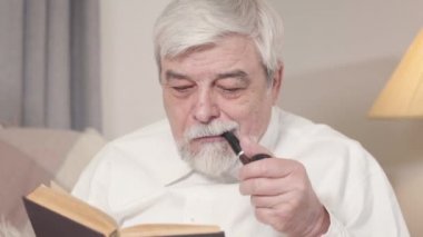 Tütün tüttüren yaşlı beyaz adamın yakın plan yüzü. Kendinden emin son sınıf öğrencisi evde mutlu bir akşam geçiriyor. Yaşam tarzı, hobi, edebiyat, boş zaman.