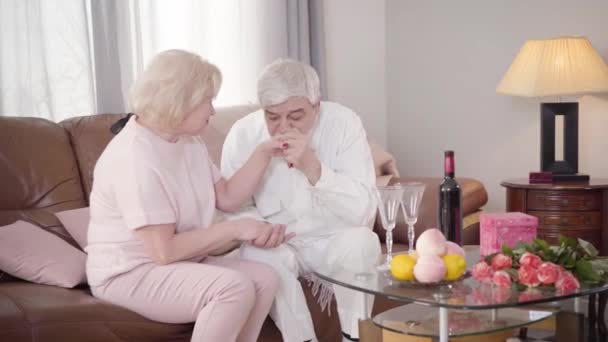 Portrait of senior Caucasian elegant man kissing womans hand and talking with wife on Saint Valentines Day. Happy old couple in love celebrating holiday at home. Lifestyle, bonding, eternal love. — Stock Video