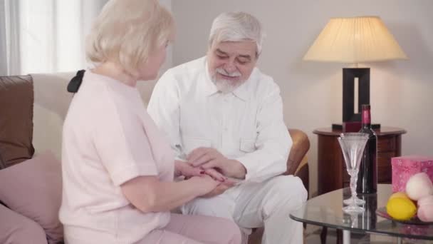 Medio tiro de feliz caucásico maduro hombre besando esposas mano y mirando a la mujer con amor. Pareja casada celebrando el día de San Valentín en casa. Vacaciones, romance, amor eterno . — Vídeo de stock