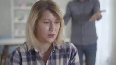 Arka planda bağıran adamı dinleyen, stresli, beyaz bir kadının yakın plan yüzü. Bunalımlı eş evde kocasıyla tartışıyor. Yaşam tarzı, evlilik sorunları, boşanma, ayrılma.