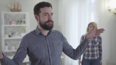 Genç sakallı beyaz adamın portresi kızgın karısının arka plana bağırışını ve duygusal hareketlerini dinliyor. Kocasıyla evde kavga eden bir kadın. Sorun, evlilik, çatışma.