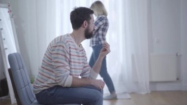 Gergin karısı arka planda yürürken genç sakallı, beyaz bir adam elinde alyansa bakıyor. Stresli evli çift ayrılıyor. Boşanma, ilişki, çatışma, ayrılık.