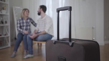 Arka planda kucaklaşan mutlu genç çift olarak ön planda duran bavulun yakın çekimi. Evli bir adam ve kadın, geziden sonra buluşuyorlar. Yaşam tarzı, evlilik, birliktelik, mutluluk..