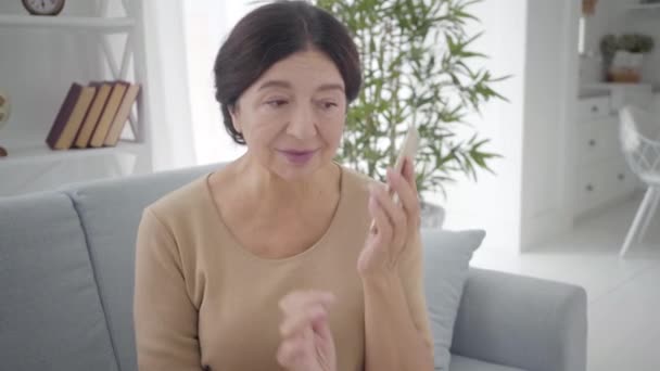 Retrato da bela mulher caucasiana sênior falando ao telefone. Senhora morena madura agradável com olhos castanhos conversando dentro de casa. Estilo de vida, beleza, tranquilidade . — Vídeo de Stock