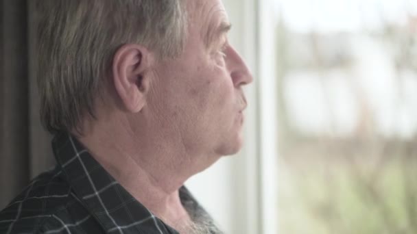 Nahaufnahme von einem reifen kaukasischen Mann, der aus dem Fenster schaut. Porträt eines männlichen Rentners im Haus. Altern, Lebensstil, Rente, Ruhestand. — Stockvideo