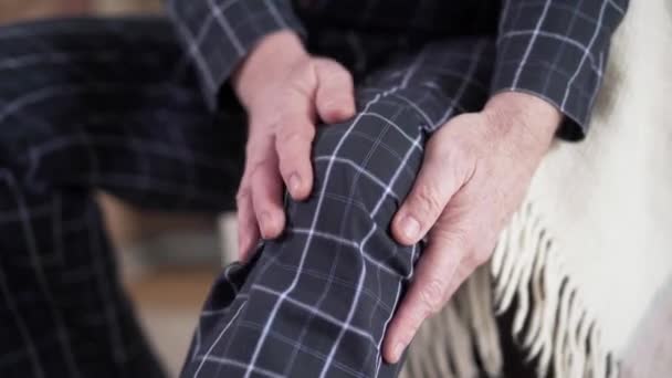 Primer plano de las manos caucásicas masculinas maduras frotando la rodilla en pijama. Jubilado mayor sufriendo de dolor. Estilo de vida, envejecimiento, problemas de salud . — Vídeo de stock