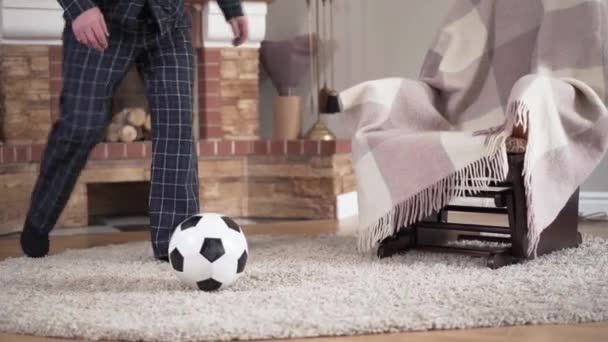 Unrecognizable Caucasian old man in pajamas hitting ball and walking away. Elderly soccer player keen on football practicing indoors at the evening. Joy, lifestyle, sport, vitality. — Stock Video