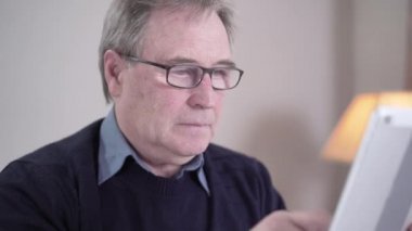 Kafkasyalı yaşlı bir adamın tablet ekranı tıklaması, gözlüğünü çıkarması ve gözlerini ovuşturması. İnternette gezinirken göz ağrısı çeken yaşlı, bitkin bir emekli. Yaşlanma, yaşam tarzı, sağlık hizmetleri.