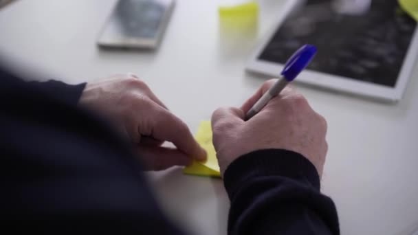 Man oude blanke handen schrijven briefje en plakken het op het boek aan de tafel. Senior mannelijke gepensioneerde vechten tegen veroudering en de ziekte van Alzheimers. Gezondheidsprobleem, neurodegeneratie, ziekte. — Stockvideo