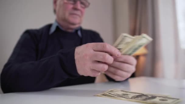 Close-up van volwassen blanke mannen die contant geld tellen en geld in aparte trossen stoppen. Wazig bezorgde gepensioneerde in bril schuddend hoofd op de achtergrond. Inkomen, armoede, armoede, pensionering. — Stockvideo