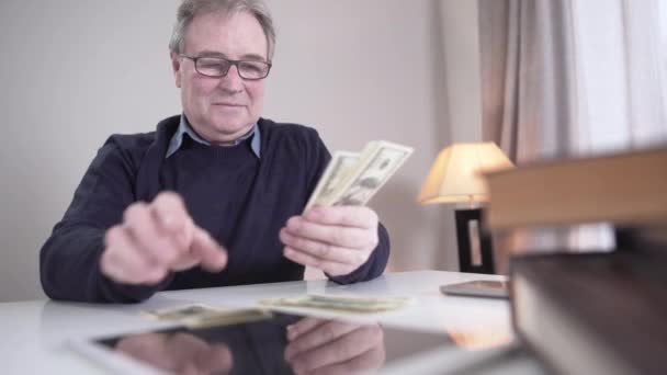 Portrait of rich old Caucasian man counting cash indoors. Smiling senior male retiree in eyeglasses calculating money at home and shaking head yes. Income, wealth, lifestyle, richness. — Stock Video