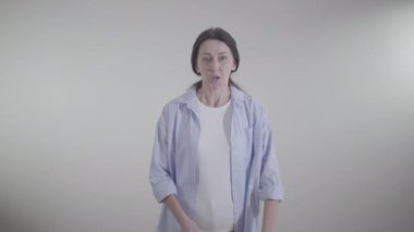 Beyaz arka planda kameraya bağıran kızgın yetişkin kadın portresi. Esmer, beyaz bayanın bağırıp çağırmasından ve duygusal hareketler yapmasından hoşnut değildi. Negatiflik, yaşam tarzı, çatışma, öfke.
