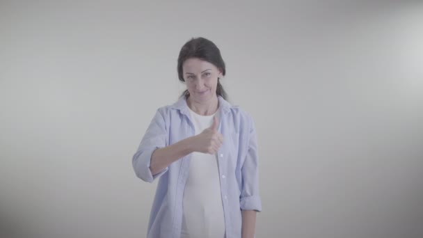 Mujer morena adulta mostrando el pulgar hacia arriba y haciendo un gesto sí agitando la cabeza. Retrato de una dama caucásica sonriente posando sobre fondo blanco. Estilo de vida, aprobación, felicidad . — Vídeo de stock