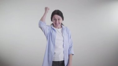 Beyaz arka planda dönüp dans eden, zafer jesti yapan heyecanlı beyaz kadın. İçeride sevinen esmer kadının portresi. Mutluluk, neşe, yaşam tarzı, güven.
