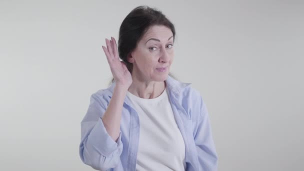 Retrato de mulher morena colocando a mão na orelha e olhando para a câmera com interesse. Senhora caucasiana positiva posando sobre fundo branco. Conceito de fofoca, rumores, audição . — Vídeo de Stock