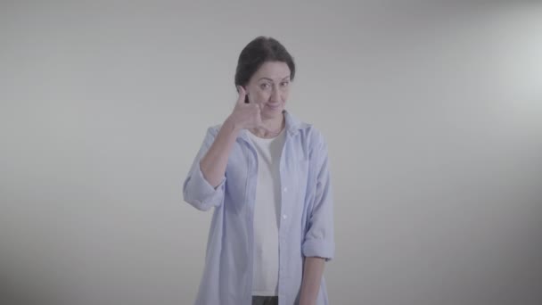 Śródokresowe ujęcie pewnej siebie kobiety pokazującej gest telefonu i gestykulującej "tak" przez potrząsanie głową. Dorosła brunetka, biała kobieta czeka na rozmowę. Styl życia, komunikacja. — Wideo stockowe