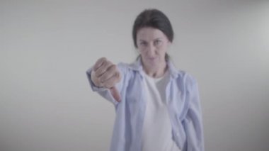 Kadın elinin baş parmağını aşağı gösteren yakın çekimi. Kafası arka planda titreyerek hayır diyen bulanık, beyaz bir kadın. Onaylamama, olumsuzluk, itiraz konsepti.