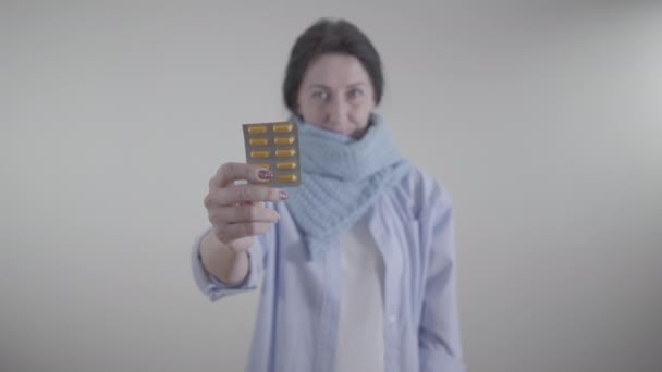 Close-up of female Caucasian hand holding blister pack of pills. Blurred adult woman in warm scarf smiling at the background. Treatment, therapy, medicine, illness. — Stock Video